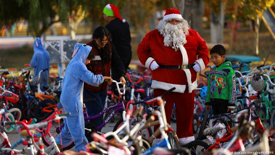 A man dressed as Santa Clause stands in the middle of a gorup of children and bicycles