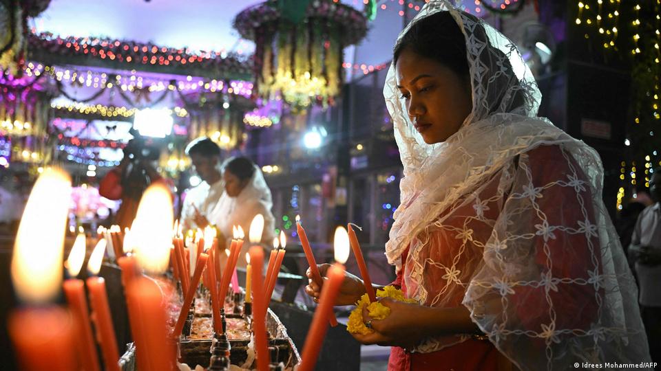 A worshiper lights a candle in amongst a number of lit candles on Dec 24, 2025