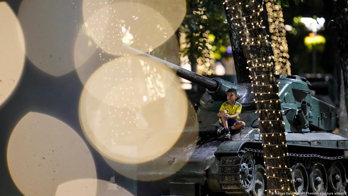 Nino sentado sobre un tanque. Alrededor, iluminación de Navidad.