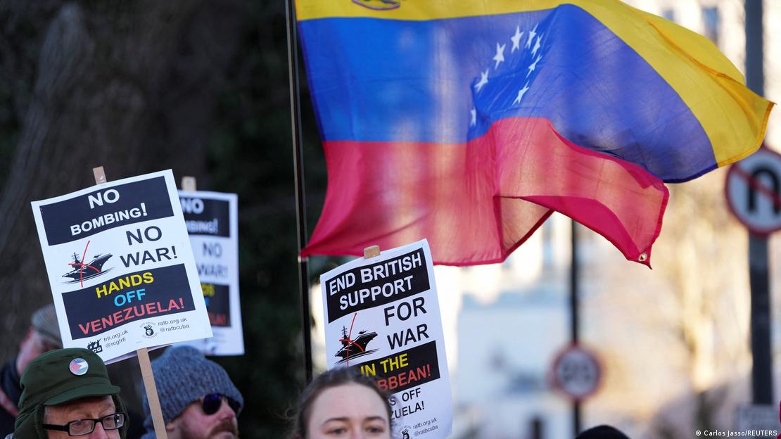 Pessoas empunham bandeira da Venezuela e cartazes com os dizeres "Sem bombardeios! Sem guerra! Tirem as mãos da Venezuela" em Londres