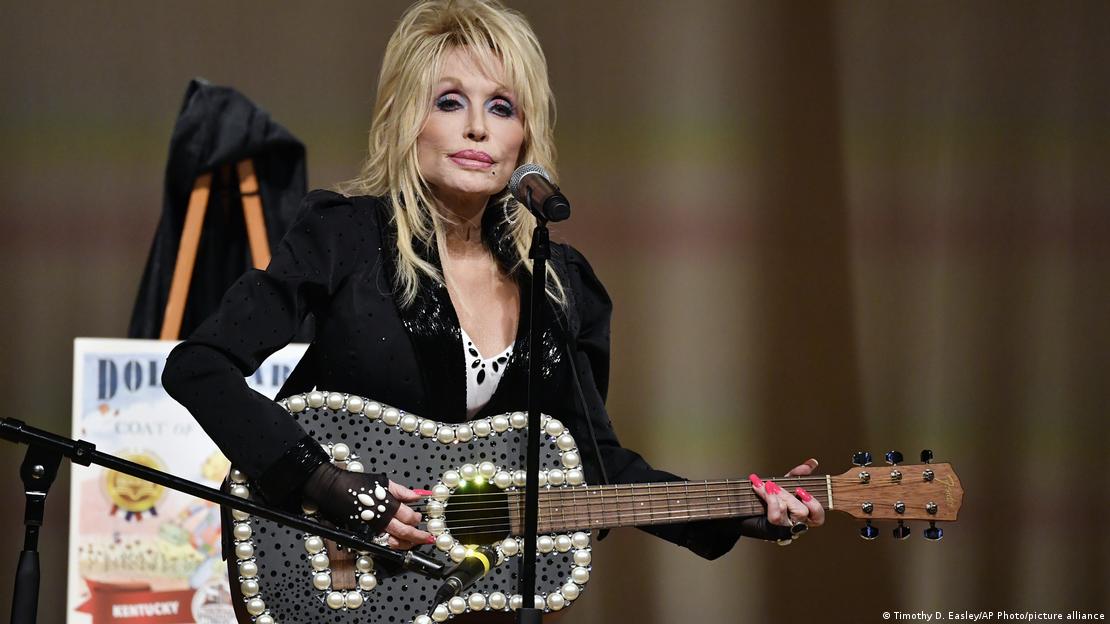 Dolly Parton playing a guitar decorated with pearls and black polka dots.