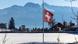 Bandeira suíça a meio mastro em frente a letreiro com o nome de Crans-Montana encoberto pela neve Bandeira suíça a meio mastro em frente a letreiro com o nome de Crans-Montana encoberto pela neve