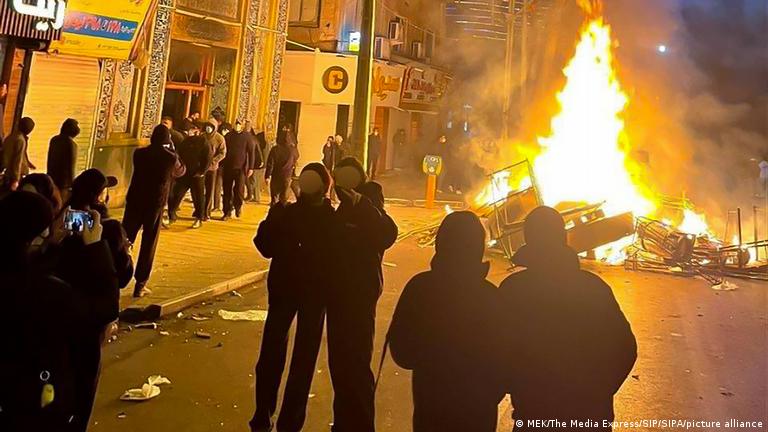 Sokakta toplanan İranlı protestocular ateşe verdikleri barikatların önünde poz verirken.