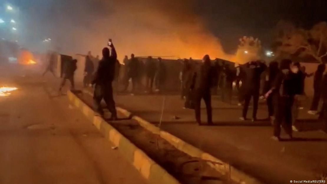 İran'ın Meşhed kentindeki hükümet karşıtı gösterilerde protestocuların arkasından dumanlar yükseliyor