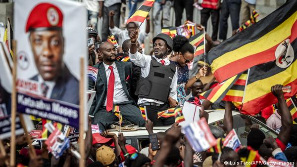 Uganda opposition leader and National Unity Platform (NUP) presidential candidate Robert Kyagulanyi Ssentamu, popularly known as Bobi Wine (C), waves a flag from atop a car as supporters cheer during his arrival to the party's final campaign rally ahead of the 2026 general elections, in Kampala