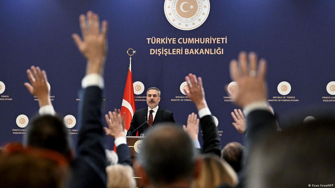 Hakan Fidan'ın toplantısı sırasında soru sormak isteyen gazetecilerin elleri görülüyor