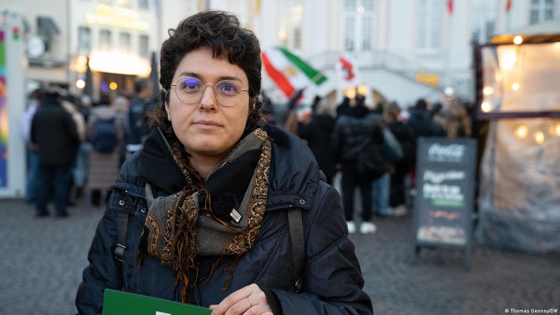 Eine Frau steht am Rande einer Protest-Demonstration gegen die iranische Regierung in Bonn und schaut ernst in die Kamera