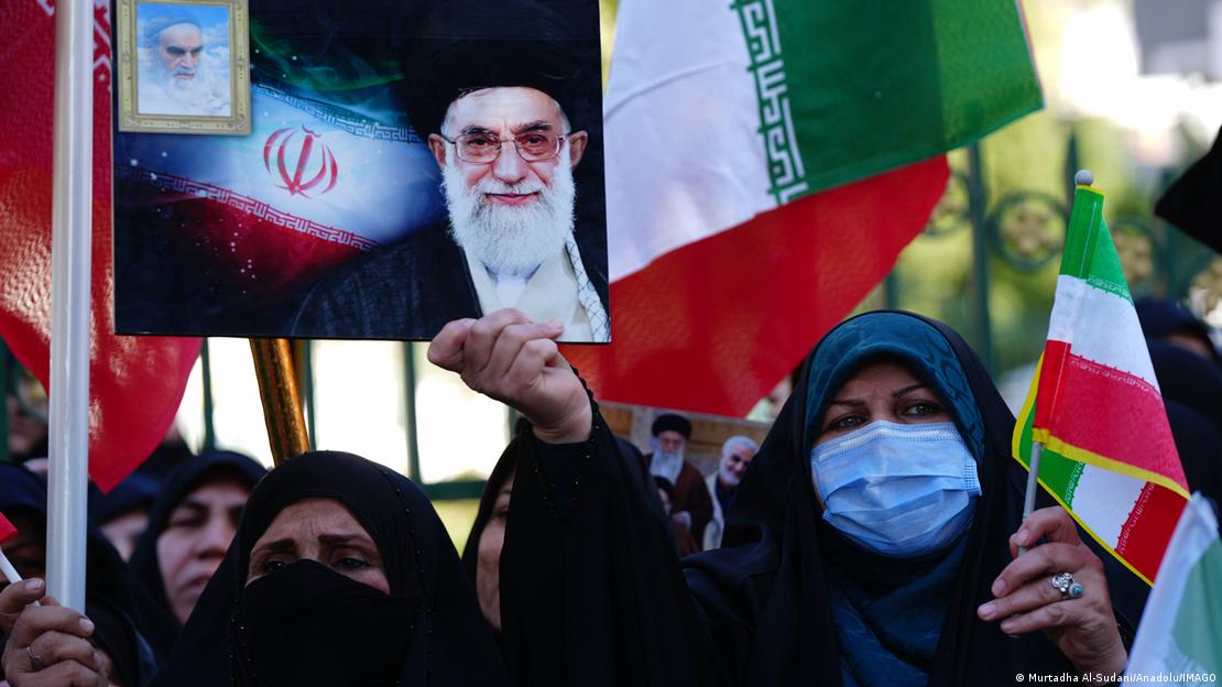 İranlı bir kadın, bir eylemde Hamaney'in fotoğrafını tutuyor, diğer eylemci kadınların elinde de İran bayrakları var 