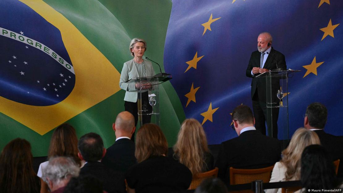 AB Komisyonu Başkanı Ursula von der Leyen, Paraguay'daki imza töreni öncesi Brezilya'ya gitti. Brezilya Devlet Başkanı Lula da Silva ile birlikte basın toplantısı yaparken görülüyor. İkisi de ayakta duruyor, arkalarındaki fon ise Brezilya ve AB bayrakları 