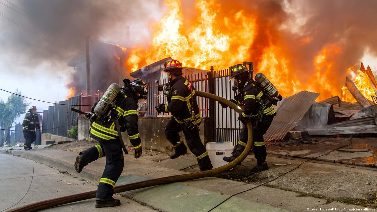 Bomberos chilenos tratan de apagar un incendio en un lugar donde hay varias viviendas.