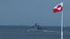 En la imagen aparece en primer plano una bandera de Groenlandia en el antiguo puerto de Nuuk y al fondo un buque de patrullaje militar danés. En la imagen aparece en primer plano una bandera de Groenlandia en el antiguo puerto de Nuuk y al fondo un buque de patrullaje militar danés.