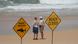 A man and a woman stand on North Steyne beach and look at the waves. Behind them, two signs read "shark sighted" and "beach closed" A man and a woman stand on North Steyne beach and look at the waves. Behind them, two signs read "shark sighted" and "beach closed"