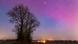 Aurora Boreal deixa céu rosa e roxo sobre campo na Dinamarca, com árvores no primeiro plano Aurora Boreal deixa céu rosa e roxo sobre campo na Dinamarca, com árvores no primeiro plano
