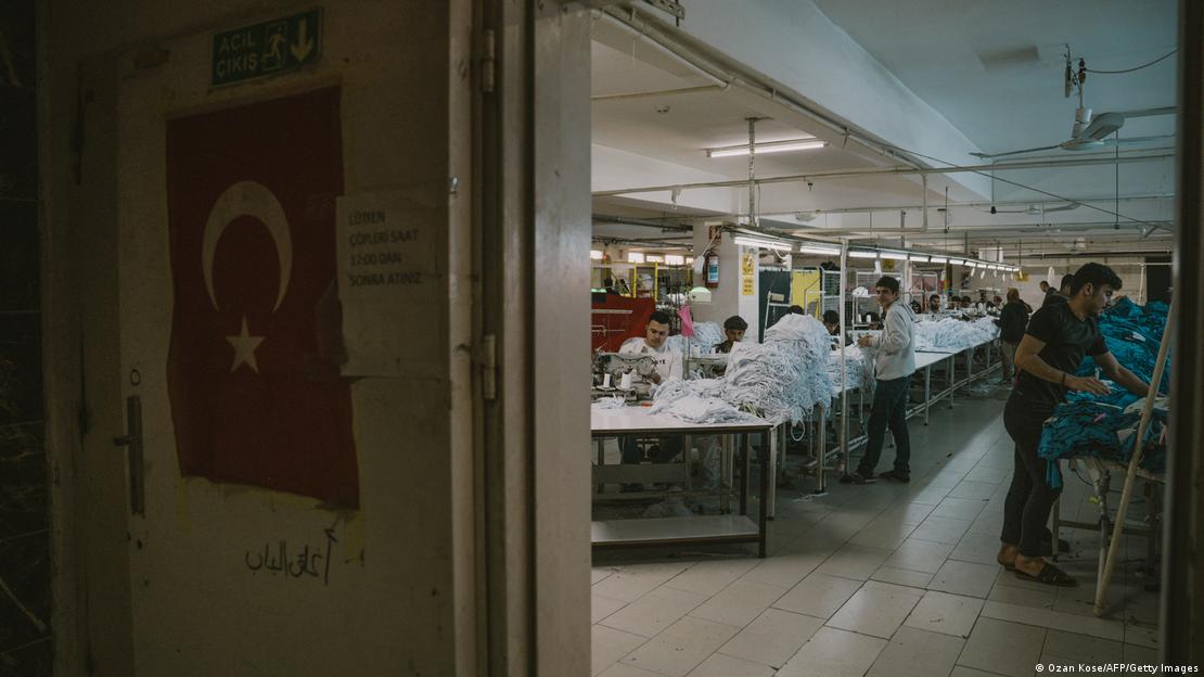 Bir tekstil üretim atölyesi. Dikiş makinelerinin başında oturan ve tekstil ürünlerini katlayan işçiler Bir tekstil üretim atölyesi. Dikiş makinelerinin başında oturan ve tekstil ürünlerini katlayan işçiler