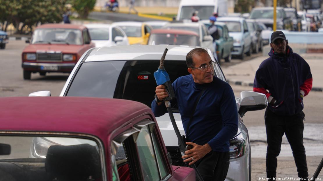 Un conductor toma el dispensador de combustible con una larga fila de automóviles detrás. Un conductor toma el dispensador de combustible con una larga fila de automóviles detrás.