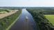 Aerial view of a cargo ship traveling through a wide canal bordered by farmland and forest areas. Aerial view of a cargo ship traveling through a wide canal bordered by farmland and forest areas.