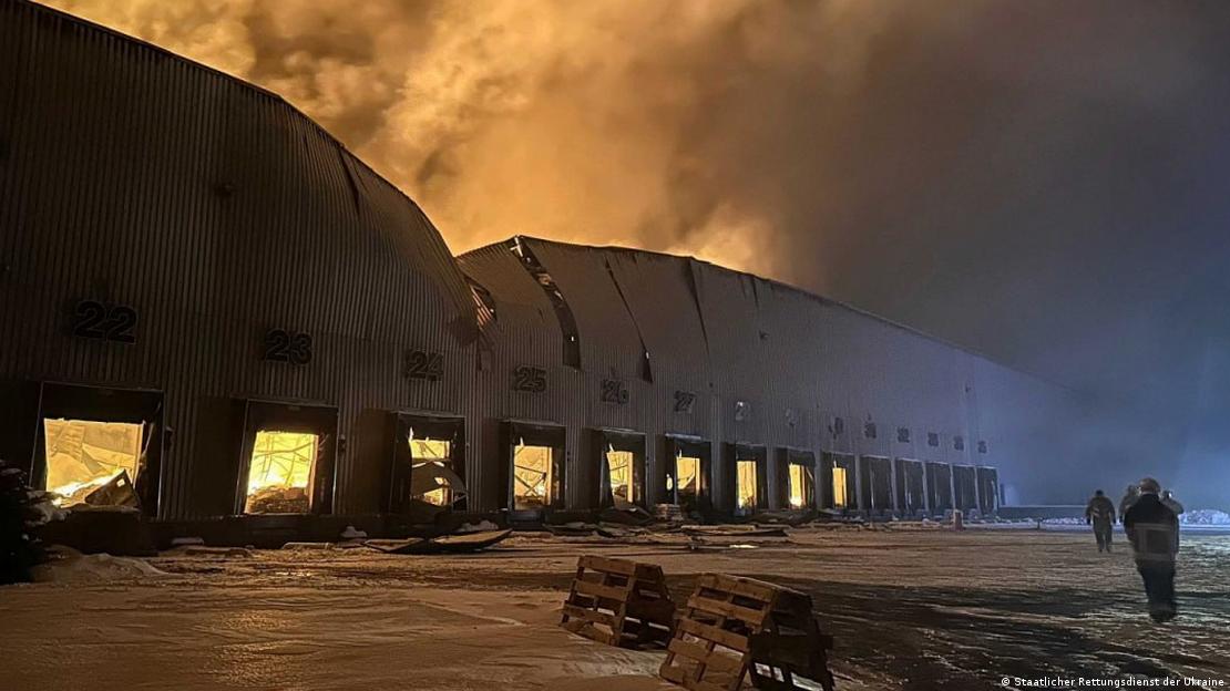 Incêndio em grande galpão, com bombeiros do lado de fora, em meio a neve