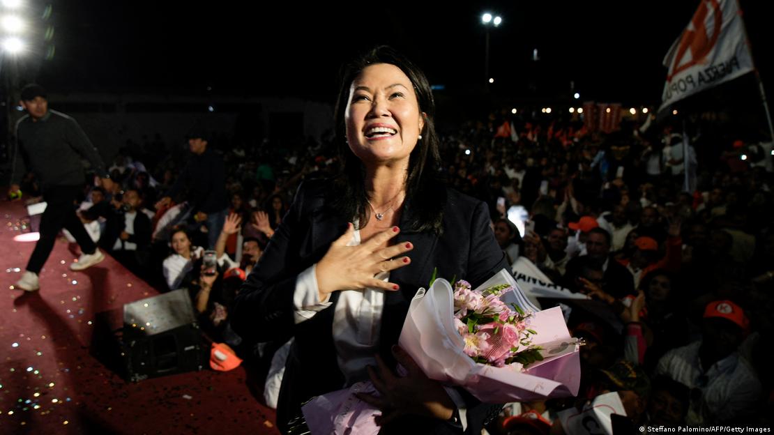 Keiko Fujimori se lleva la mano derecha al pecho. En la izquierda sostiene un ramo de flores. Sonríe y detrás de ella hay muchos simpatizantes.