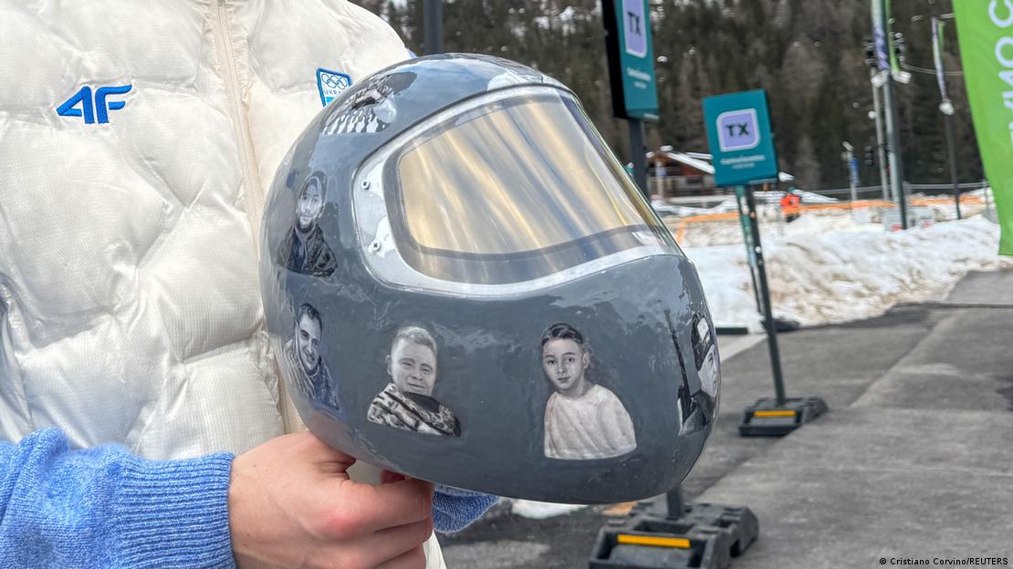 Juegos Olímpicos de Invierno de Milán-Cortina 2026 | Un atleta ucraniano de skeleton sostiene en sus manos su casco gris con fotos de los atletas caídos en la guerra tras la invasión rusa de Ucrania.