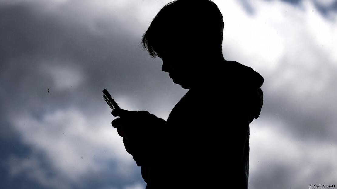 Karanlık bulutların altında elindeki akıllı telefona bakan bir çocuğun silüeti
