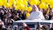 Pope Leo XIV, man in white vestments looking over cabin of popemobile in front of crowd with many yellow balloons Pope Leo XIV, man in white vestments looking over cabin of popemobile in front of crowd with many yellow balloons