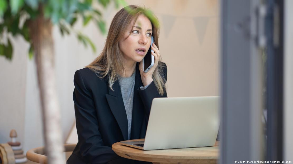 Evden çalışan bir kadın, önünde bilgisayarı telefonda konuşuyor