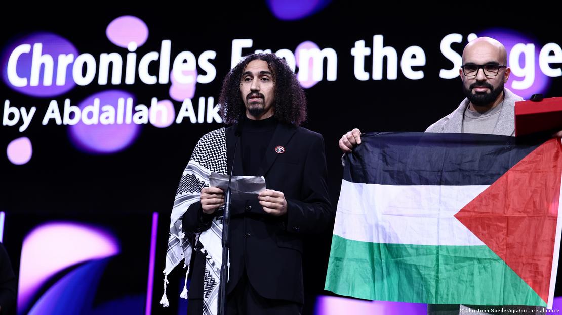 El cineasta Abdallah Alkhatib da un discurso en la ceremonia de premiación de la Berlinale, alguien a su lado sostiene la bandera palestina. El cineasta Abdallah Alkhatib da un discurso en la ceremonia de premiación de la Berlinale, alguien a su lado sostiene la bandera palestina.