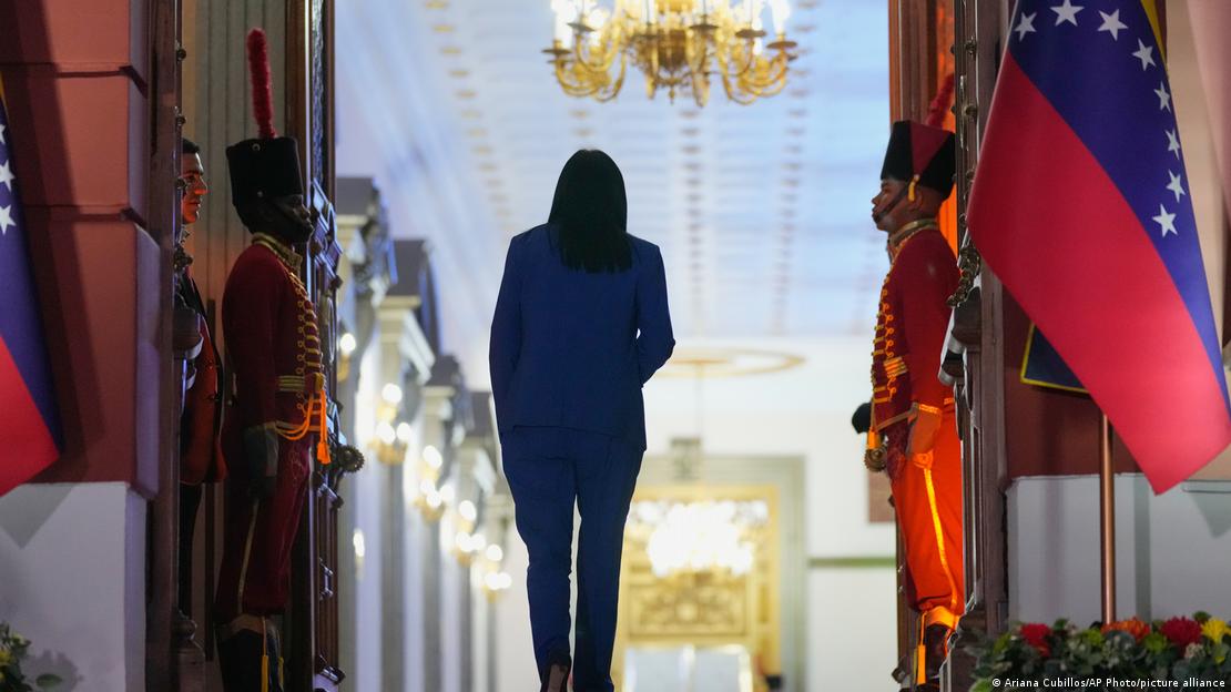 Delcy Rodríguez camina de espaldas, flanqueada por soldados y banderas de Venezuela. Delcy Rodríguez camina de espaldas, flanqueada por soldados y banderas de Venezuela.