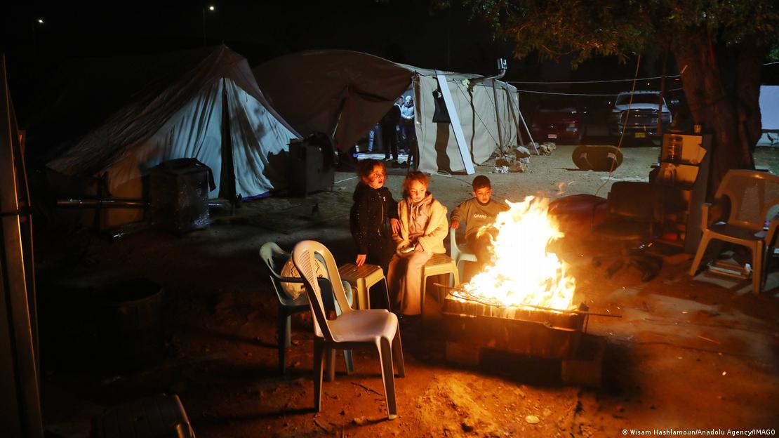 Em meio a abrigos improvisados, crianças se aquecem perto de uma fogueira