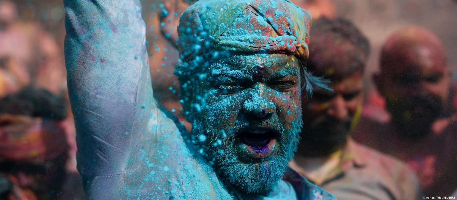 A close-up view shows a bearded man; his face and clothing are blue in color, he is raising one arm and his mouth is wide open.