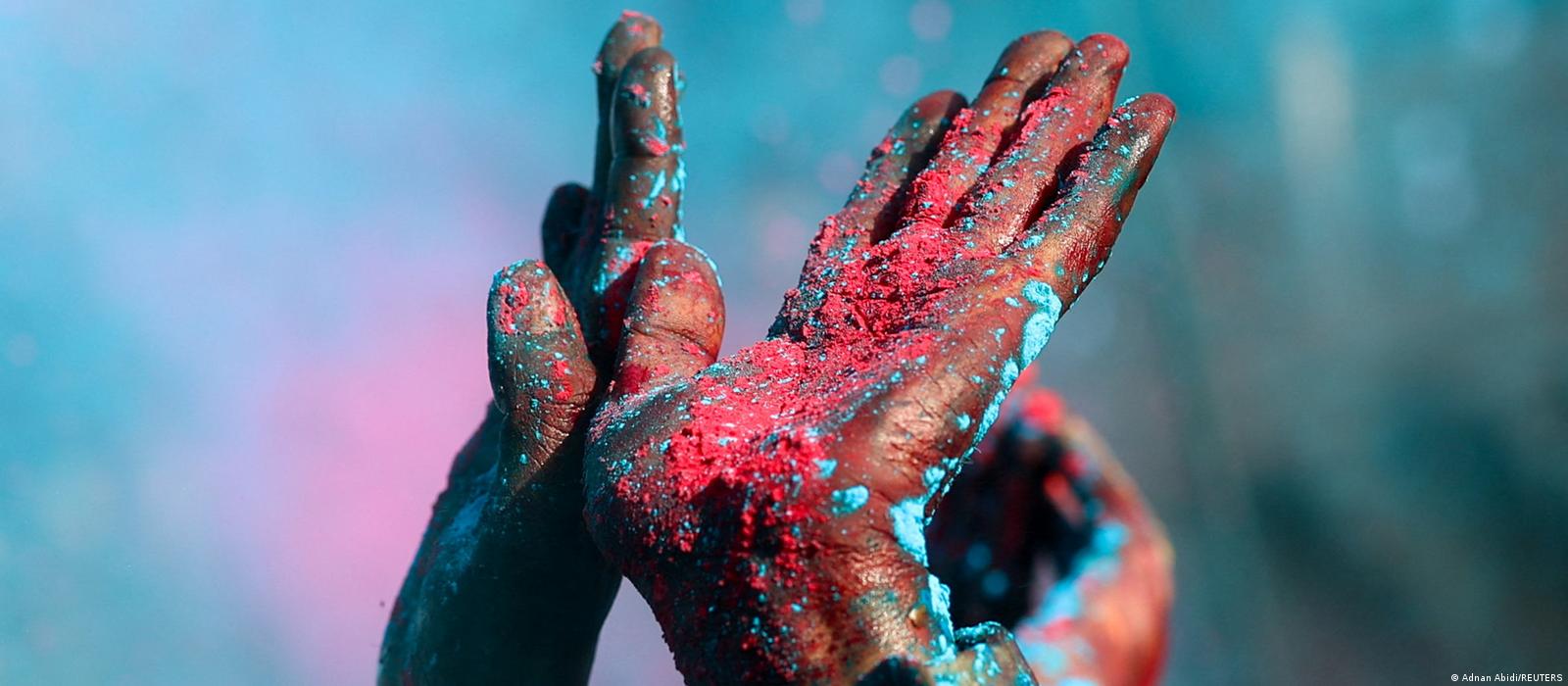 A close-up shows two hands held up in the air. They are covered all over with blue and red pigments.