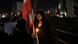 Con una vela y una bandera iraní, una mujer vestida de negro y cubierta con el velo islámico llora. Al fondo, otros manifestantes que no se distinguen.
