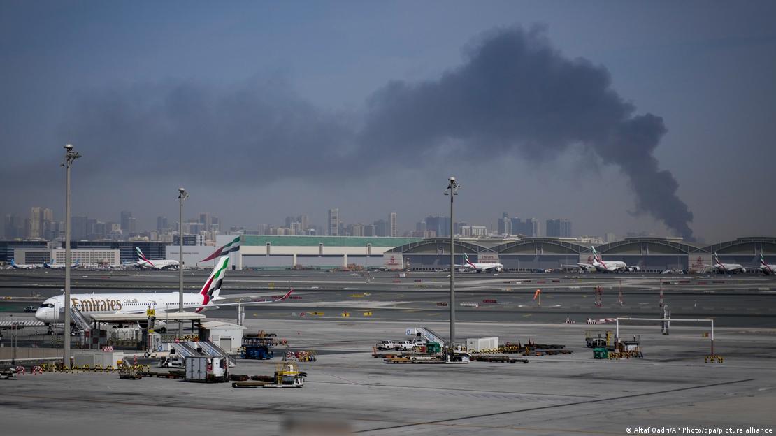 Una columna de huma se eleva fondo provocada por un ataque iraní, mientras los aviones de Emirates permanecen en tierra en el Aeropuerto Internacional de Dubai tras el cierre de la terminal.