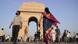People walking and gathering in front of India Gate in New Delhi under a clear sky; in the foreground a woman in a colorful sari and a man passing by the historic war memorial. People walking and gathering in front of India Gate in New Delhi under a clear sky; in the foreground a woman in a colorful sari and a man passing by the historic war memorial.