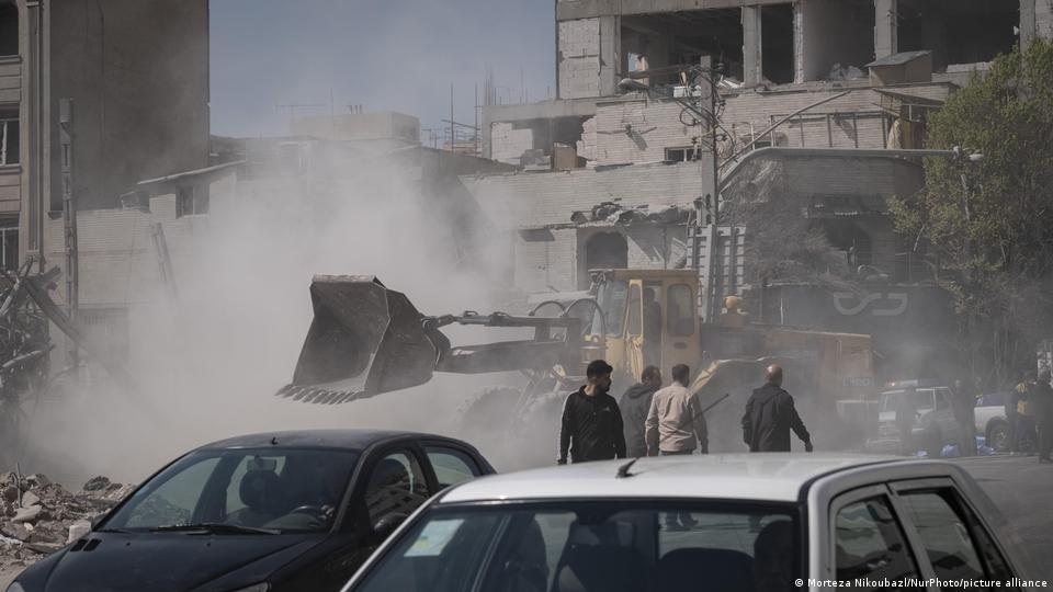 Tahran'da ABD-İsrail saldırılarında yıkılan bir binanın enkazı temizleniyor. Fotoğrafta bir iş makinesi ve önünde bekleyen kişiler görülüyor