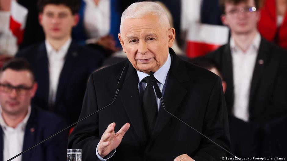 Muž (Jaroslaw Kaczynski) gestikuluje při projevu u řečnického pultu. V pozadí jsou lidé. Krakov, Polsko, 7. března 2026.