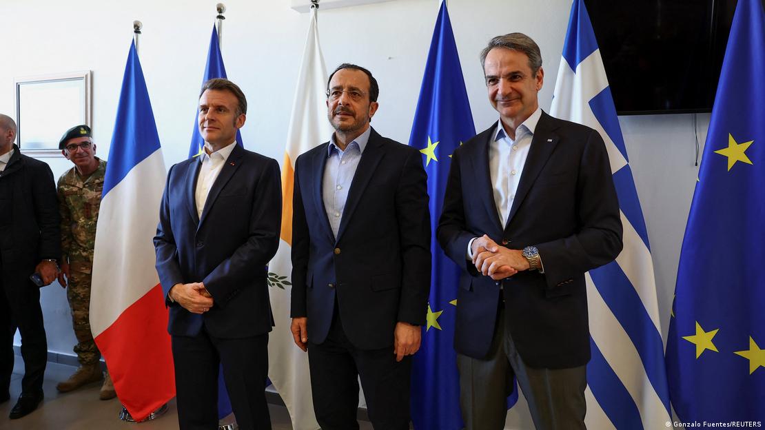 Fransa Cumhurbaşkanı Emanuel Macron, Yunanistan Başbakanı Kiryakos Mitsotakis ve Güney Kıbrıs lideri Hristodulidis, üç ülke ve AB bayrakları önünde duruyor. 