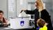A woman drops a ballot into a ballot box marked with the flag of Slovenia at a polling station in Ljubljana, Slovenia on March 17, 2026. Behind the box, another woman is seated at a table. In the foreground, a child looks on A woman drops a ballot into a ballot box marked with the flag of Slovenia at a polling station in Ljubljana, Slovenia on March 17, 2026. Behind the box, another woman is seated at a table. In the foreground, a child looks on