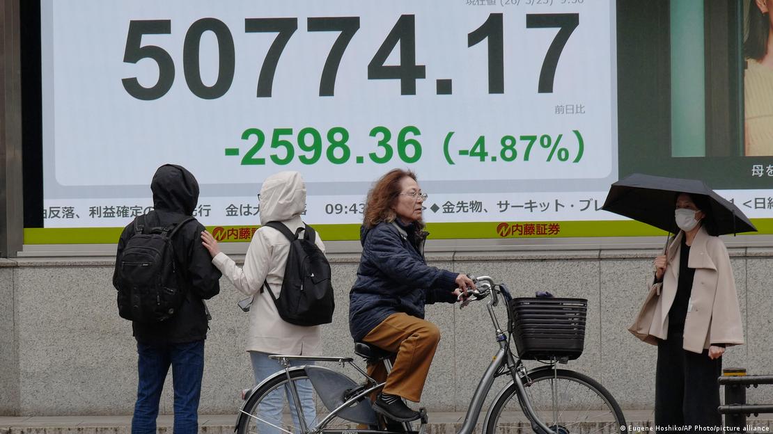 People stand in front of an electronic stock board showing Japan's Nikkei index at a securities firm Monday, March 23, 2026, in Tokyo. 