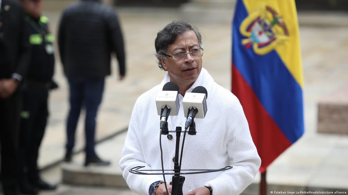 Gustavo Petro ante micrófonos y una bandera colombiana.