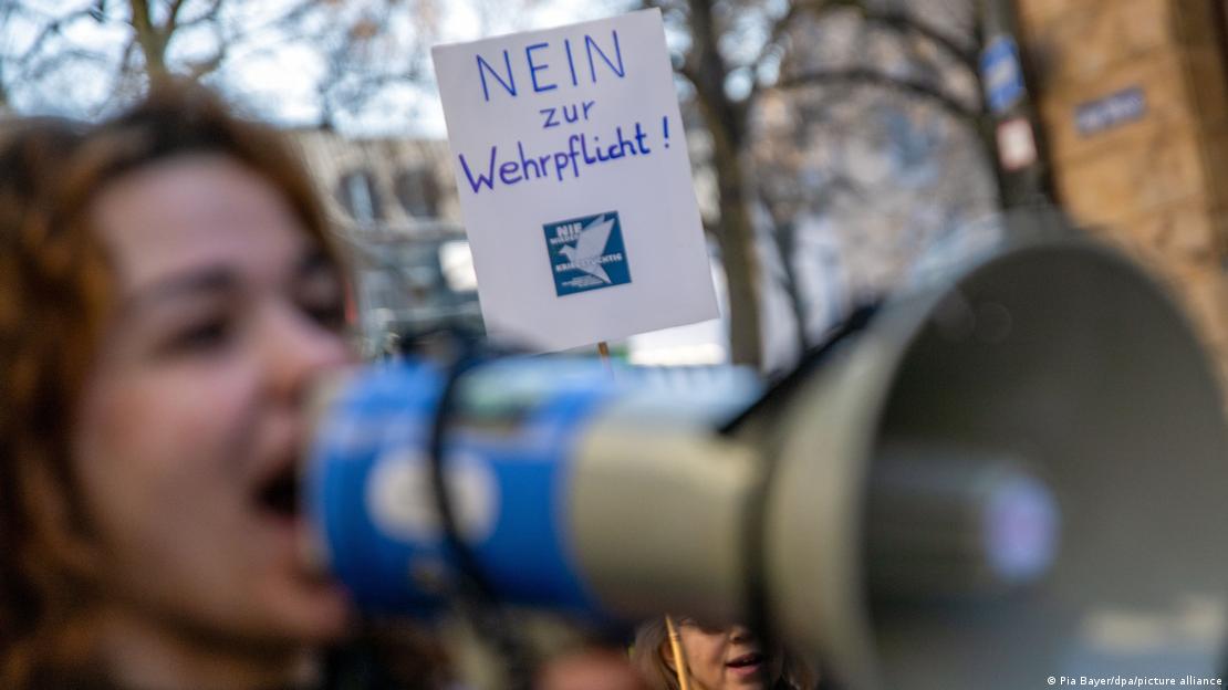 "Nein zur Wehrpflicht!" (Zorunlu askerliğe hayır) yazılı bir pankartın önünde megafondan seslenen genç bir gösterici kadın