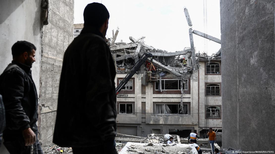 Tahran'da ABD-İsrail'in hava saldırısında hasar almış bir binaya doğru bakan iki kişi