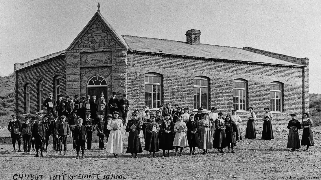 Personas posando ante una escuela. Imagen en blanco y negro.