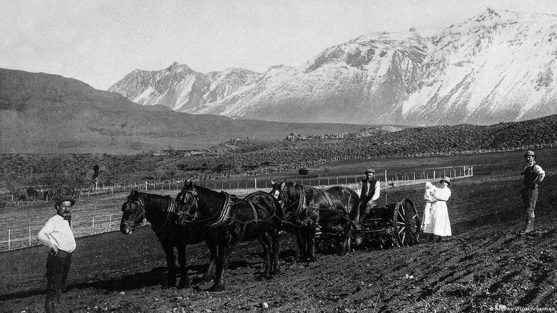 Carro tirado por caballos en un campo. De fondo, grandes montes.