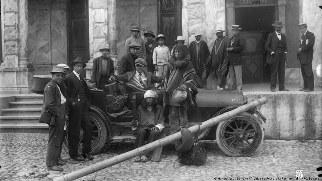 Imagen en blanco y negro. Personas posando junto a un vehículo antiguo.