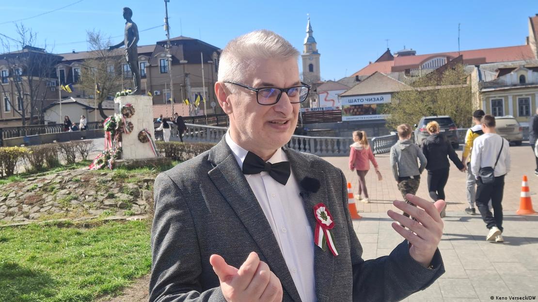 Ein Mann in Anzug (Laszlo Zubanics) spricht, hinter ihm ein Denkmal, an dessen Sockel Kränze mit Bändern in den Farben der ungarischen Fahne liegen