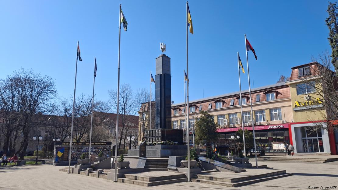 El momumento, una columna cuadrangular culminada con el escudo ucraniano dorado, en un pedestal con escaleras y rodeado de banderas, sobre el que hay coronas de flores y placas de mármol con los nombres de los caídos. El momumento, una columna cuadrangular culminada con el escudo ucraniano dorado, en un pedestal con escaleras y rodeado de banderas, sobre el que hay coronas de flores y placas de mármol con los nombres de los caídos.