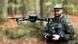 Mali dron na oko metar i po od zemlje dok se u pozadini vidi nemački vojnik koji njime upravlja Mali dron na oko metar i po od zemlje dok se u pozadini vidi nemački vojnik koji njime upravlja