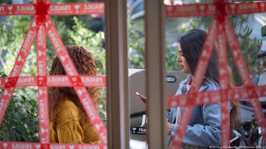 Irã, Teerã, 2026 | O dia a dia na guerra | Duas jovens em frente a um café com janelas cobertas com fita adesiva Irã, Teerã, 2026 | O dia a dia na guerra | Duas jovens em frente a um café com janelas cobertas com fita adesiva