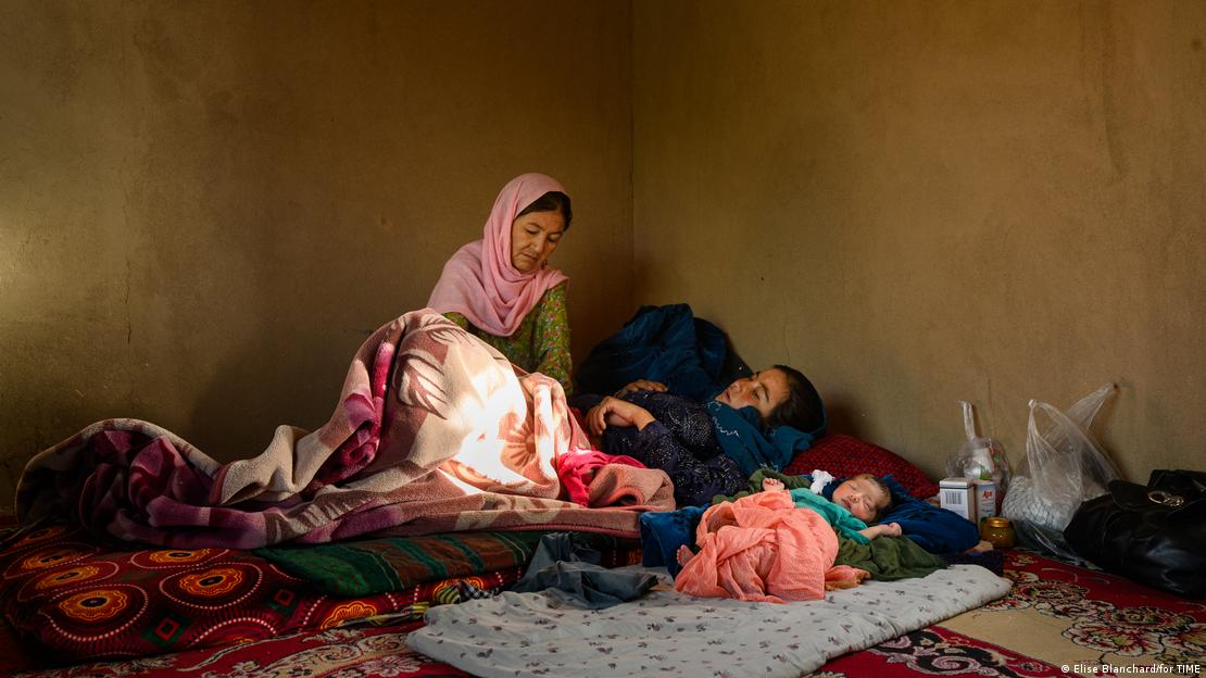 اس تصویر میں افغانستان کے ایک گھر کے پسماندہ سے کمرے میں ایک بیمار خاتون کا ایک دیگر خاتون معائنہ کرتی دکھائی دے رہی ہیں جبکہ ایک چھوٹا بچہ بھی ان کے ساتھ زمین پر لگے بستر پر سو رہا ہے